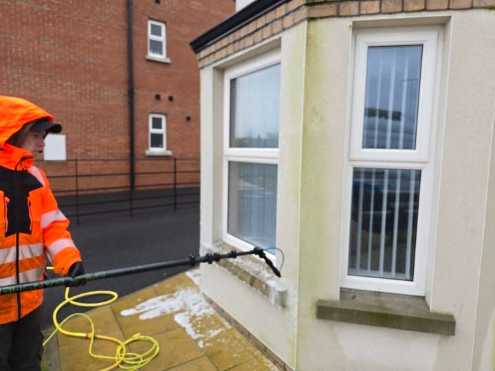 Whitehouse Outdoor Services technician in hi-vis gear softwashing an exterior wall in Northern Ireland